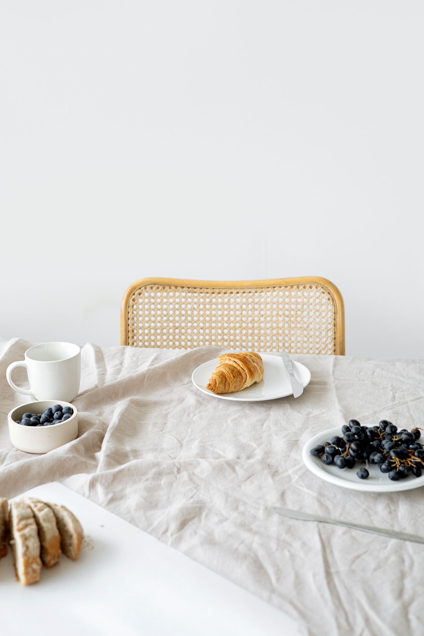 A light-filled table with bread, fruit and a croissant